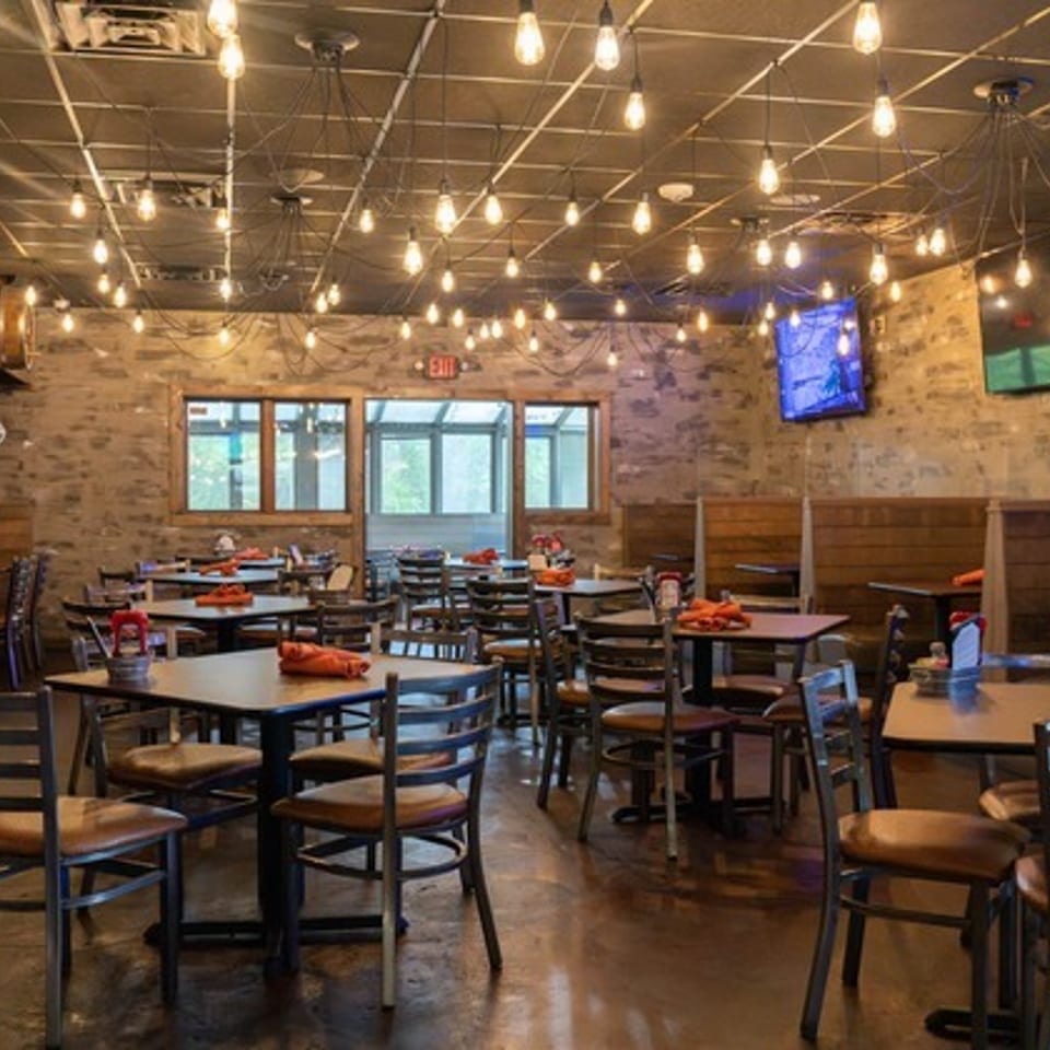 Rustic restaurant dining room with wooden booths, set tables, barrel décor, pendant lights, and wall-mounted televisions.