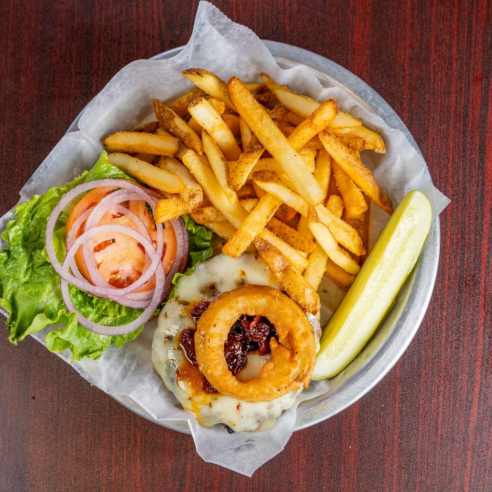 Cheeseburger topped with bacon and onion rings, served with golden fries, lettuce, tomato, onions, and a pickle spear.