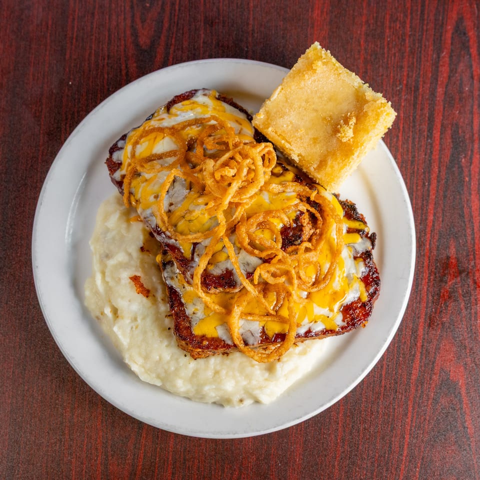 Cheeseburger topped with crispy fried onions, served over mashed potatoes with a square of golden cornbread.
